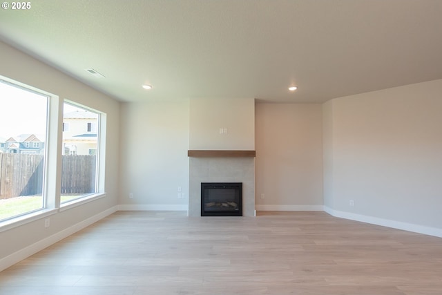 unfurnished living room with a tile fireplace, a healthy amount of sunlight, light wood-type flooring, and recessed lighting