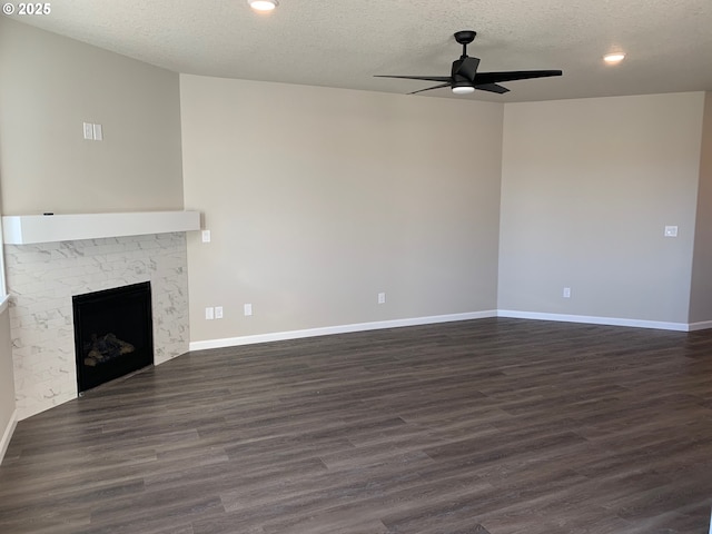 unfurnished living room with dark wood-type flooring, ceiling fan, a fireplace, and a textured ceiling