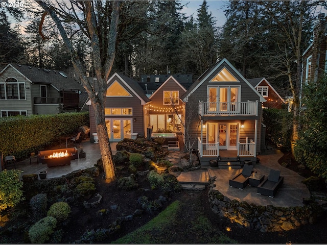 back house at dusk with a balcony, a patio, and an outdoor living space with a fire pit