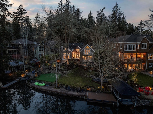 back house at dusk with a water view, a balcony, and a yard