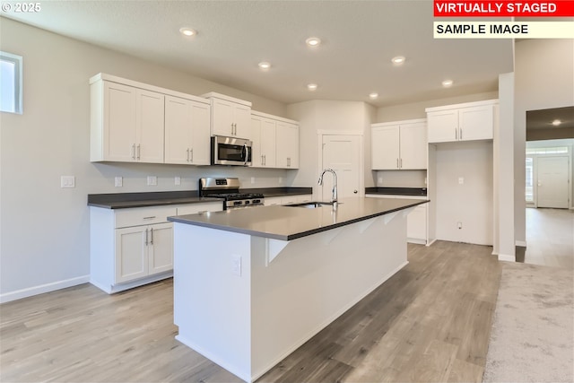 kitchen featuring recessed lighting, dark countertops, white cabinets, appliances with stainless steel finishes, and a sink