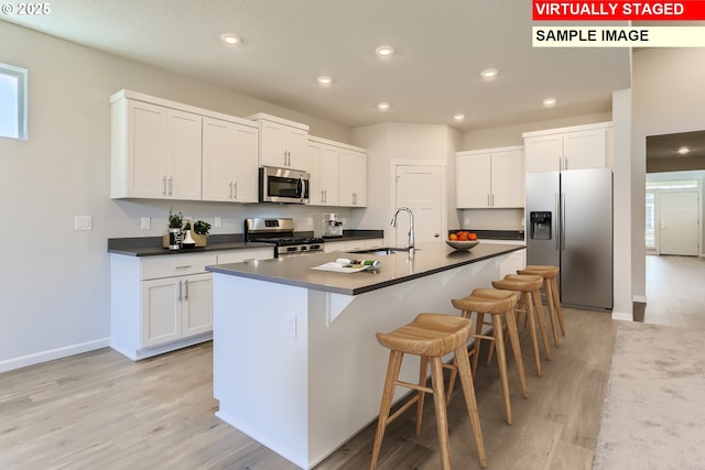 kitchen featuring white cabinets, a sink, appliances with stainless steel finishes, a kitchen breakfast bar, and dark countertops