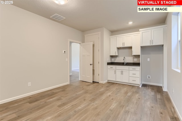 kitchen with visible vents, baseboards, light wood-style flooring, and dark countertops