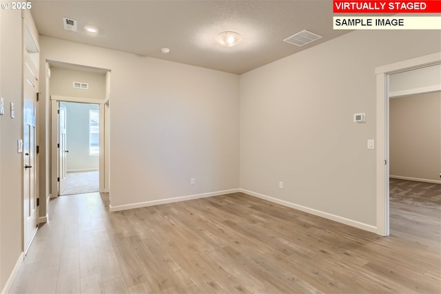 empty room featuring visible vents, light wood-style flooring, baseboards, and a textured ceiling