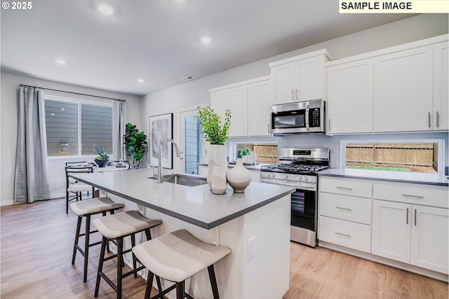 9388 SW Vermillion Dr Unit H235, Tualatin, OR 97062 - kitchen featuring appliances with stainless steel finishes, light wood-style floors, a center island with sink, recessed lighting, and white cabinets