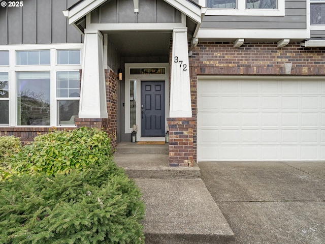 entrance to property featuring brick siding, driveway, an attached garage, and board and batten siding