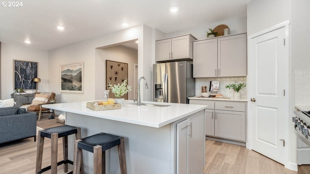 kitchen with a kitchen breakfast bar, appliances with stainless steel finishes, backsplash, a center island with sink, and light hardwood / wood-style floors