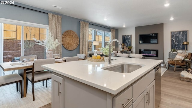 kitchen with white cabinetry, an island with sink, sink, light wood-type flooring, and stainless steel dishwasher