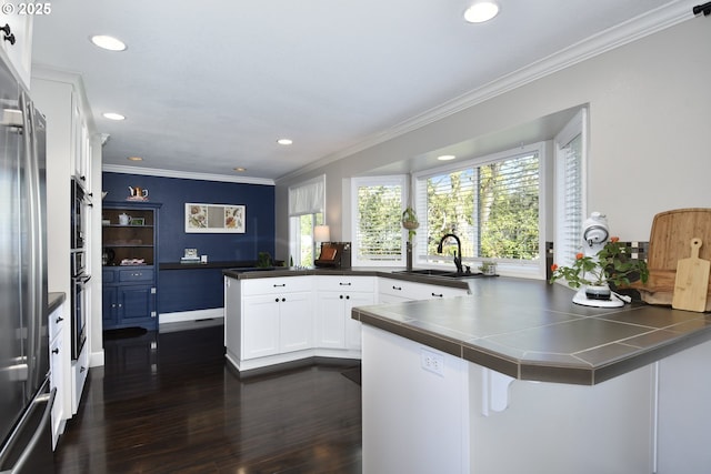 kitchen with a peninsula, a sink, stainless steel fridge, crown molding, and dark wood-type flooring