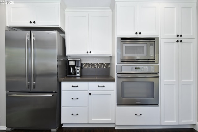 kitchen with stainless steel appliances, white cabinetry, dark countertops, and tasteful backsplash
