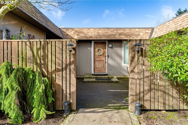 view of exterior entry featuring fence and roof with shingles