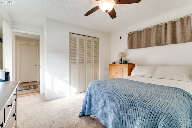 bedroom featuring a textured ceiling, a ceiling fan, a closet, and light colored carpet