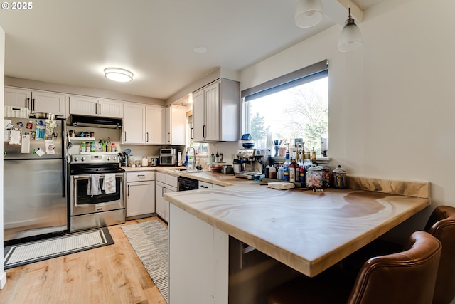 kitchen with under cabinet range hood, stainless steel appliances, a peninsula, a sink, and light countertops