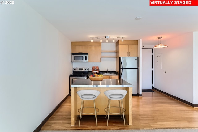 kitchen featuring a breakfast bar area, light wood finished floors, appliances with stainless steel finishes, light brown cabinets, and baseboards