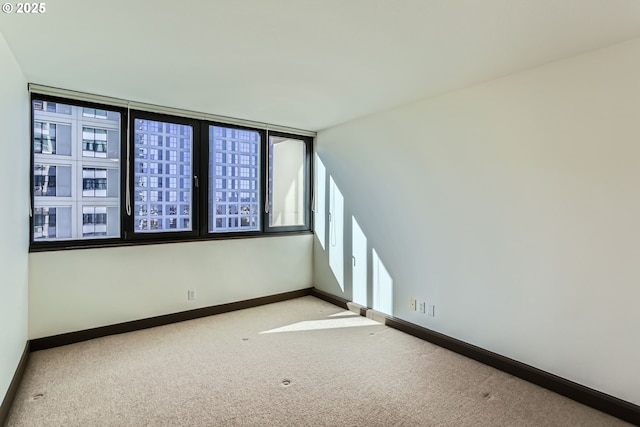 spare room with baseboards and light colored carpet