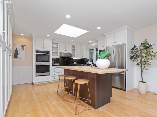 kitchen with white cabinetry, appliances with stainless steel finishes, an island with sink, and a kitchen bar