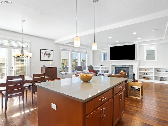 kitchen with a tile fireplace, a kitchen island, pendant lighting, and dark hardwood / wood-style flooring