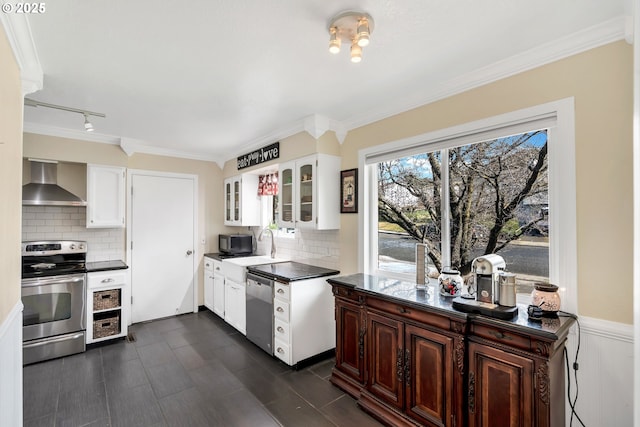 kitchen with dark countertops, appliances with stainless steel finishes, glass insert cabinets, white cabinetry, and wall chimney exhaust hood