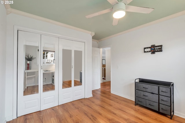 bedroom featuring wood finished floors, a ceiling fan, baseboards, a closet, and crown molding