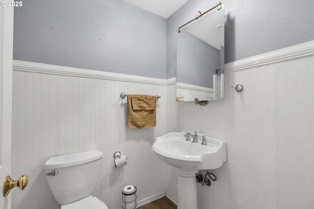 half bathroom with wainscoting, a sink, and toilet