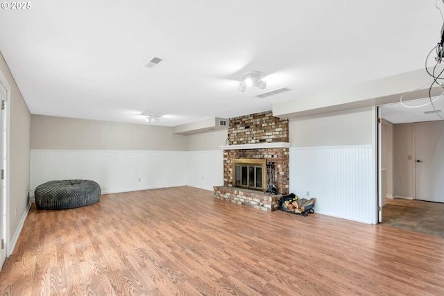 unfurnished living room with a brick fireplace, a wainscoted wall, visible vents, and wood finished floors