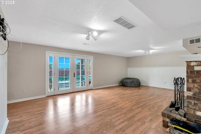 living area with a brick fireplace, visible vents, wood finished floors, and french doors