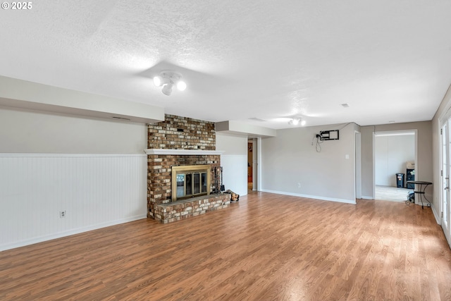 unfurnished living room with a fireplace, a textured ceiling, baseboards, and wood finished floors