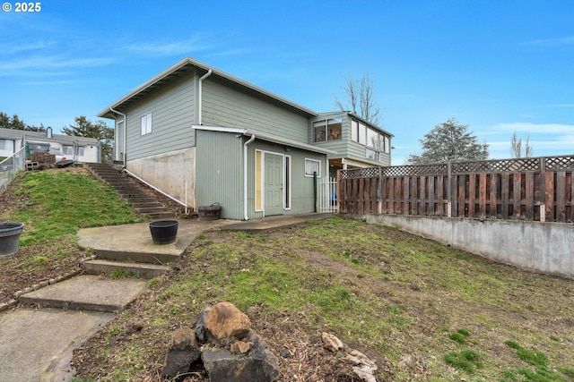 rear view of property featuring fence, stairway, a lawn, and a patio