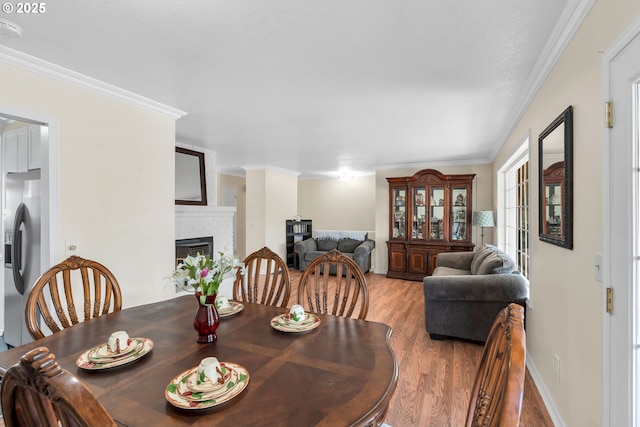 dining space with crown molding, a fireplace, baseboards, and wood finished floors