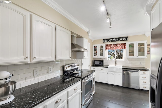 kitchen with appliances with stainless steel finishes, ornamental molding, white cabinetry, a sink, and wall chimney exhaust hood