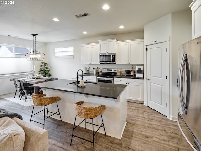 kitchen with sink, appliances with stainless steel finishes, pendant lighting, a kitchen island with sink, and white cabinets