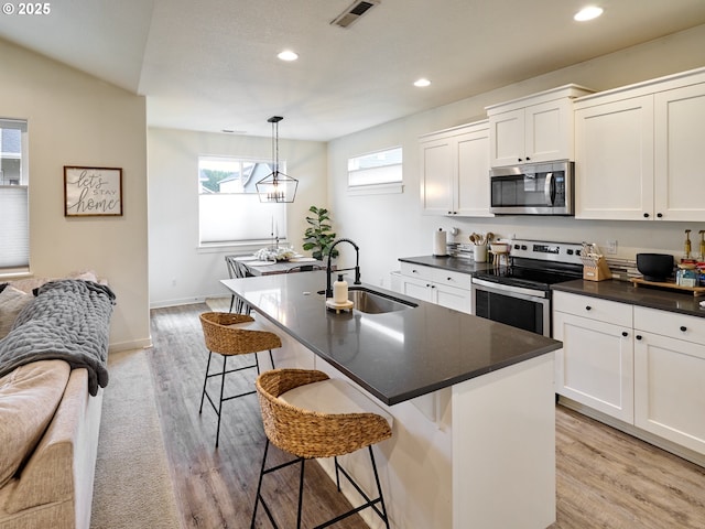 kitchen with appliances with stainless steel finishes, a kitchen bar, a kitchen island with sink, and hanging light fixtures