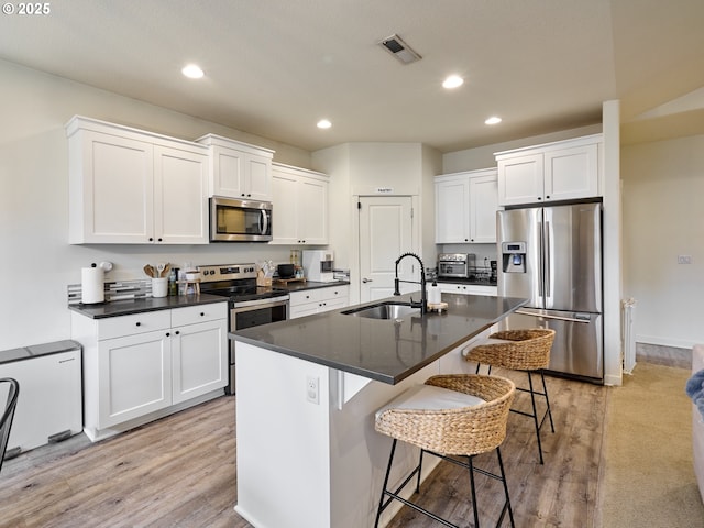 kitchen featuring appliances with stainless steel finishes, a sink, dark countertops, a kitchen breakfast bar, and recessed lighting