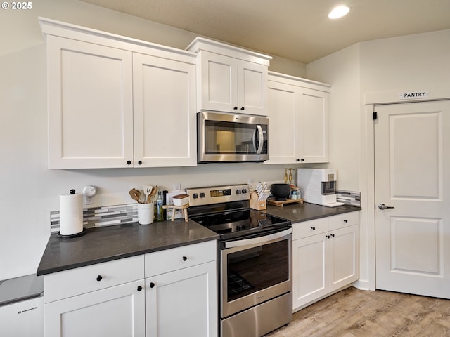 kitchen with stainless steel appliances, dark countertops, recessed lighting, white cabinetry, and light wood finished floors