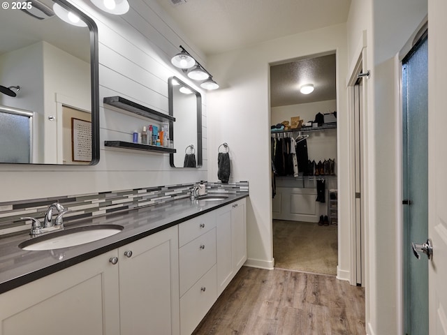 full bathroom featuring wood finished floors, double vanity, a spacious closet, baseboards, and tasteful backsplash