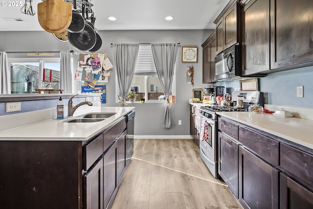 kitchen featuring light wood-style flooring, a sink, dark brown cabinetry, light countertops, and gas range