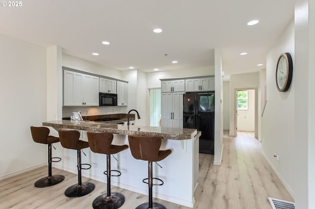 10372 NW Forestview Way, Portland, OR 97229 - kitchen with black appliances, a peninsula, dark stone counters, a breakfast bar, and recessed lighting