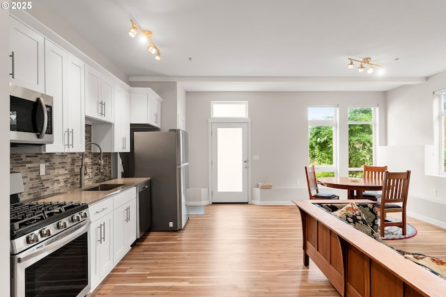 2021 SE Clinton St Unit 103, Portland, OR 97202 - kitchen featuring appliances with stainless steel finishes, light wood finished floors, tasteful backsplash, and track lighting