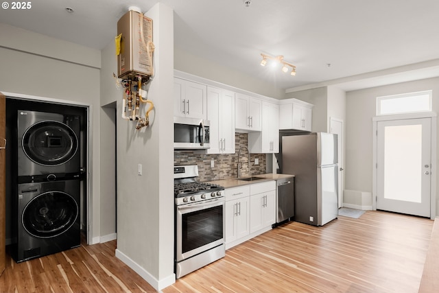 2021 SE Clinton St Unit 103, Portland, OR 97202 - kitchen featuring stainless steel appliances, estacked washer and dryer, tasteful backsplash, light wood-style floors, and white cabinetry