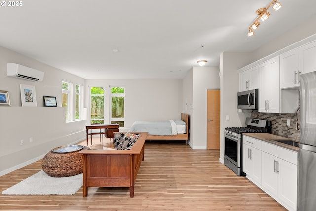 2021 SE Clinton St Unit 103, Portland, OR 97202 - kitchen featuring appliances with stainless steel finishes, a wall mounted air conditioner, light wood-style flooring, tasteful backsplash, and white cabinets