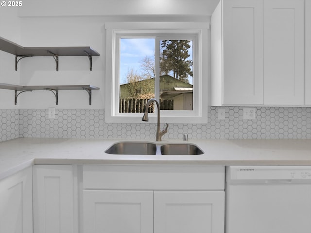 kitchen featuring white cabinets, dishwasher, backsplash, light countertops, and a sink