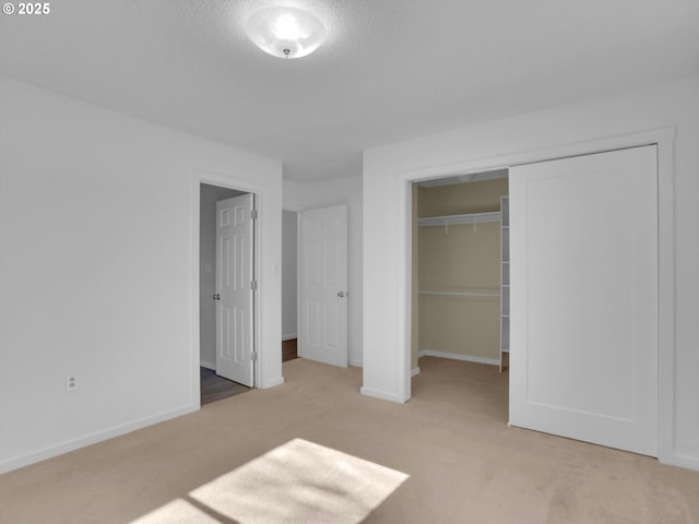 unfurnished bedroom with light carpet, a textured ceiling, baseboards, and a closet