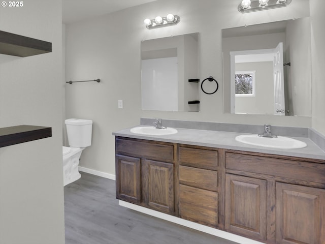 bathroom with wood finished floors, a sink, toilet, and double vanity