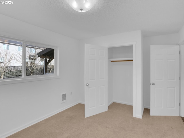 unfurnished bedroom with baseboards, a textured ceiling, visible vents, and light colored carpet