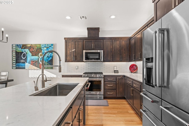 kitchen with sink, light stone counters, tasteful backsplash, light wood-type flooring, and stainless steel appliances