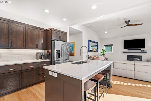 kitchen with a breakfast bar, high end fridge, sink, a center island with sink, and light hardwood / wood-style floors