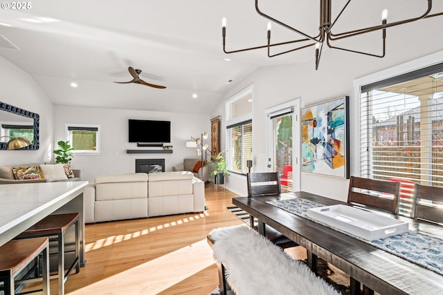 dining area with vaulted ceiling, ceiling fan with notable chandelier, a wealth of natural light, and light hardwood / wood-style flooring