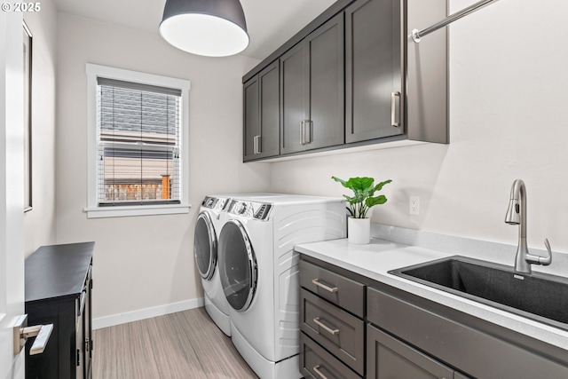 laundry room featuring washer and dryer, sink, light hardwood / wood-style floors, and cabinets