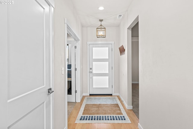 doorway to outside with a notable chandelier and light wood-type flooring