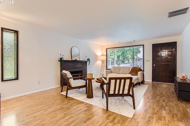 living area with light wood-style flooring, a brick fireplace, and baseboards